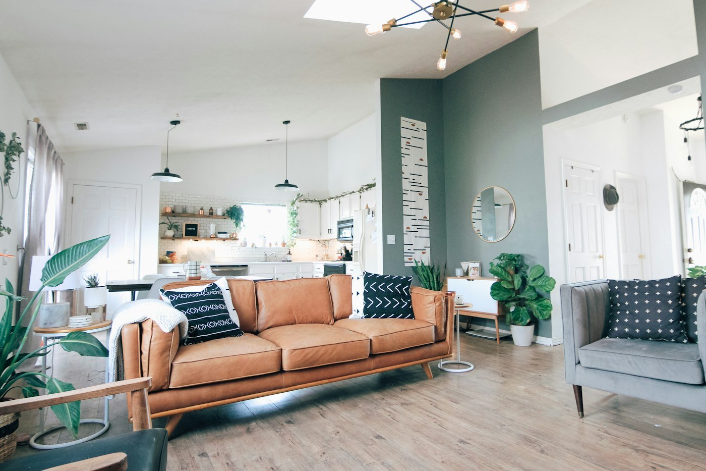 An open living room with a brown leather sofa, a grey chair, and a kitchen beyond